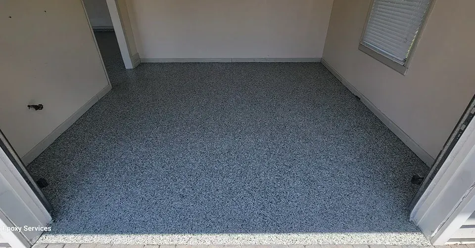 Epoxy-coated garage floor, speckled blue-gray, with light beige walls and a window.
