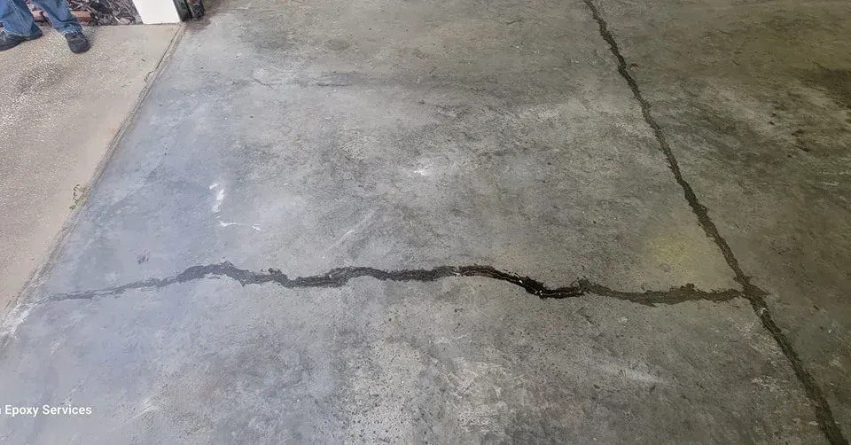 Concrete floor with a long, dark crack filled with a liquid.