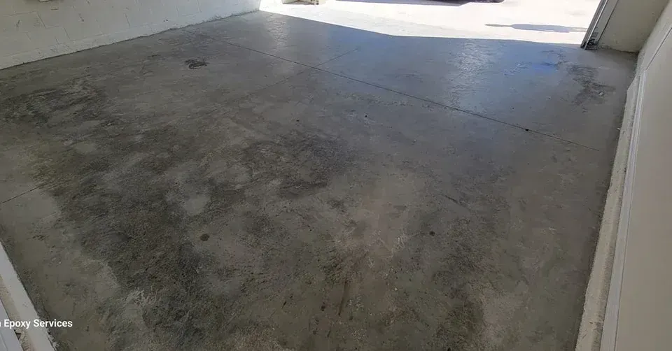 Concrete floor in a mostly empty space with some discoloration and vehicle tire tracks.
