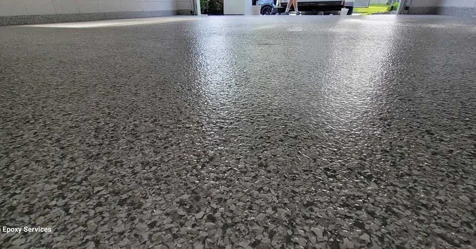 Epoxy-coated garage floor with flecks. Sunlight reflects off the glossy, gray surface.