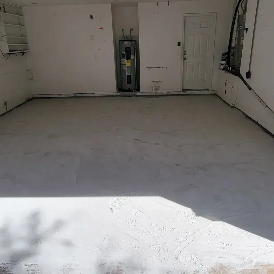 Empty, freshly painted white garage floor. Concrete walls, door, water heater, and a window are visible.