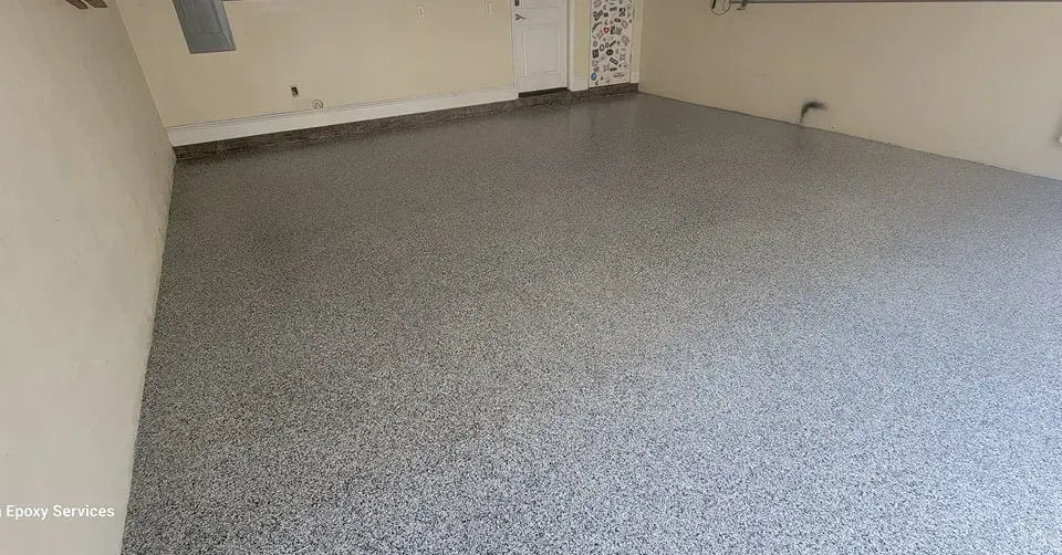 Garage with gray speckled epoxy flooring. Empty, cream-colored walls. Door in the background.