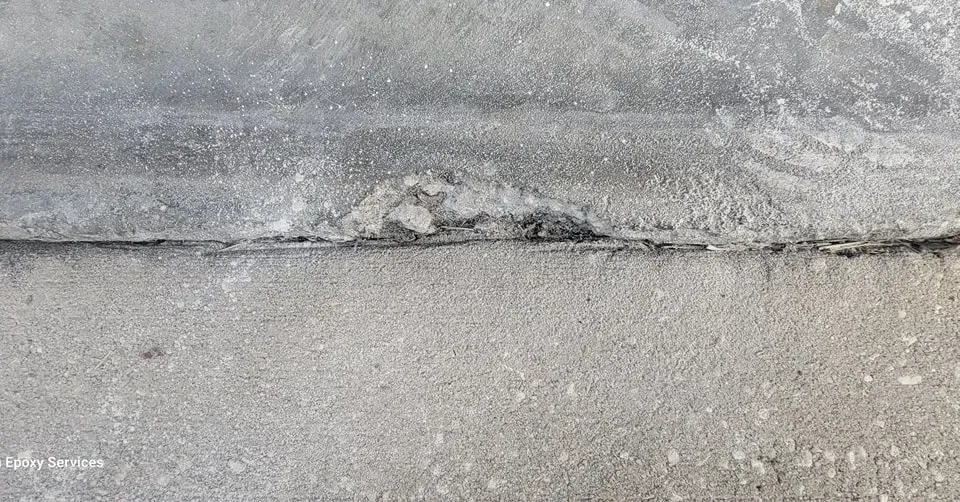 Close-up of a concrete surface with a damaged area and a visible seam between the concrete sections.