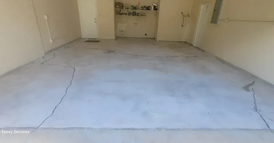 Cracked concrete floor in a room with light-colored walls and a doorway in the background.
