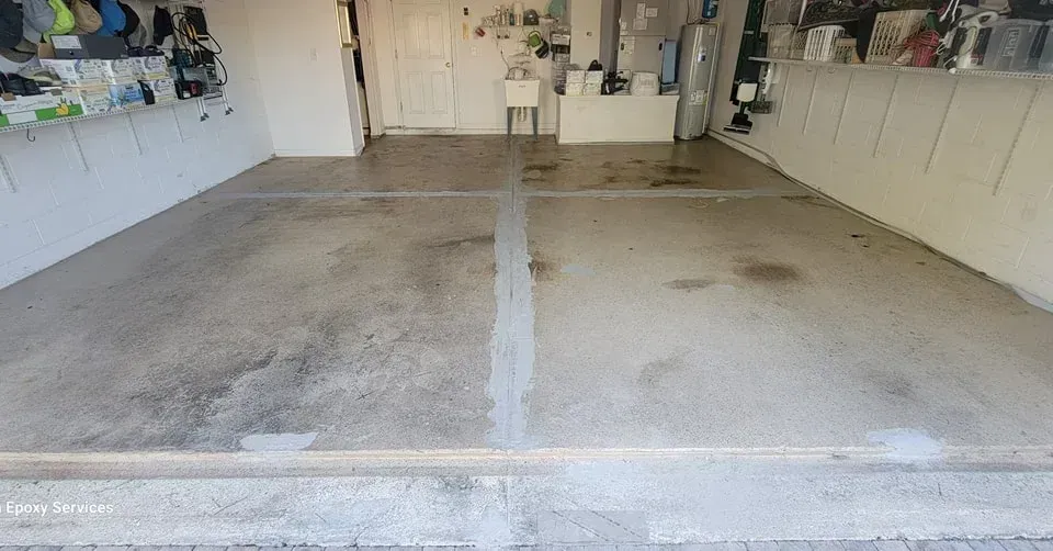 Garage interior, concrete floor, visible stains, open door, white walls, overhead storage.
