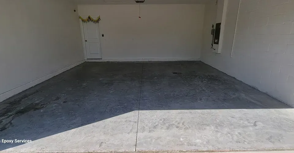 Empty, gray-floored garage with white walls, a closed door, and a light fixture on the ceiling.