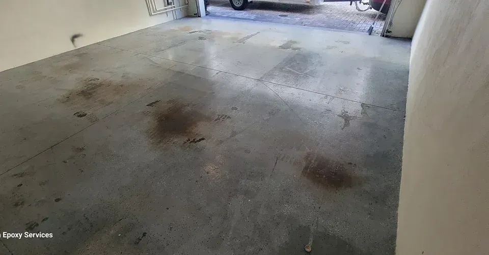 Garage floor with dark stains, possibly oil, and a partially visible vehicle outside.