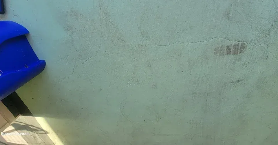 Blue object against a worn, yellowish-green wall, with cracks and stains visible.