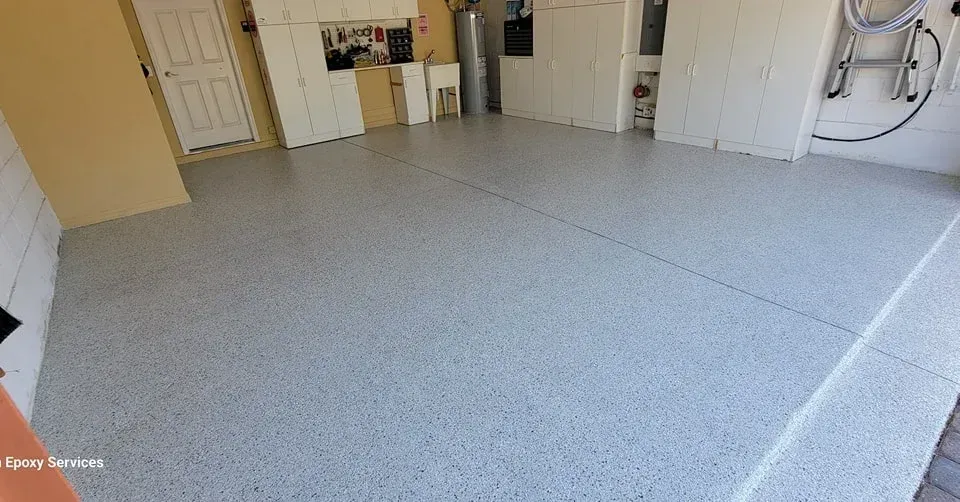 Garage with speckled gray epoxy flooring, white cabinets, and closed door.