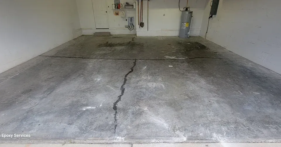 Empty garage with cracked concrete floor, water heater, and utility pipes visible.