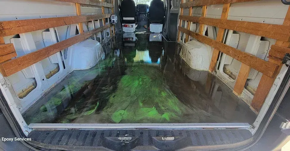 Interior of a white van with a glowing green and black epoxy floor, with wood shelving.