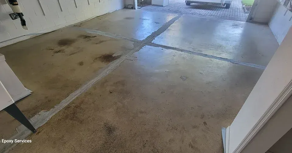 Garage floor, concrete with visible cracks, some dark stains, and reflected light.