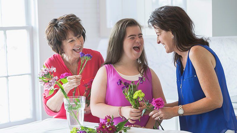 Two women and a younger woman laugh and hold flowers