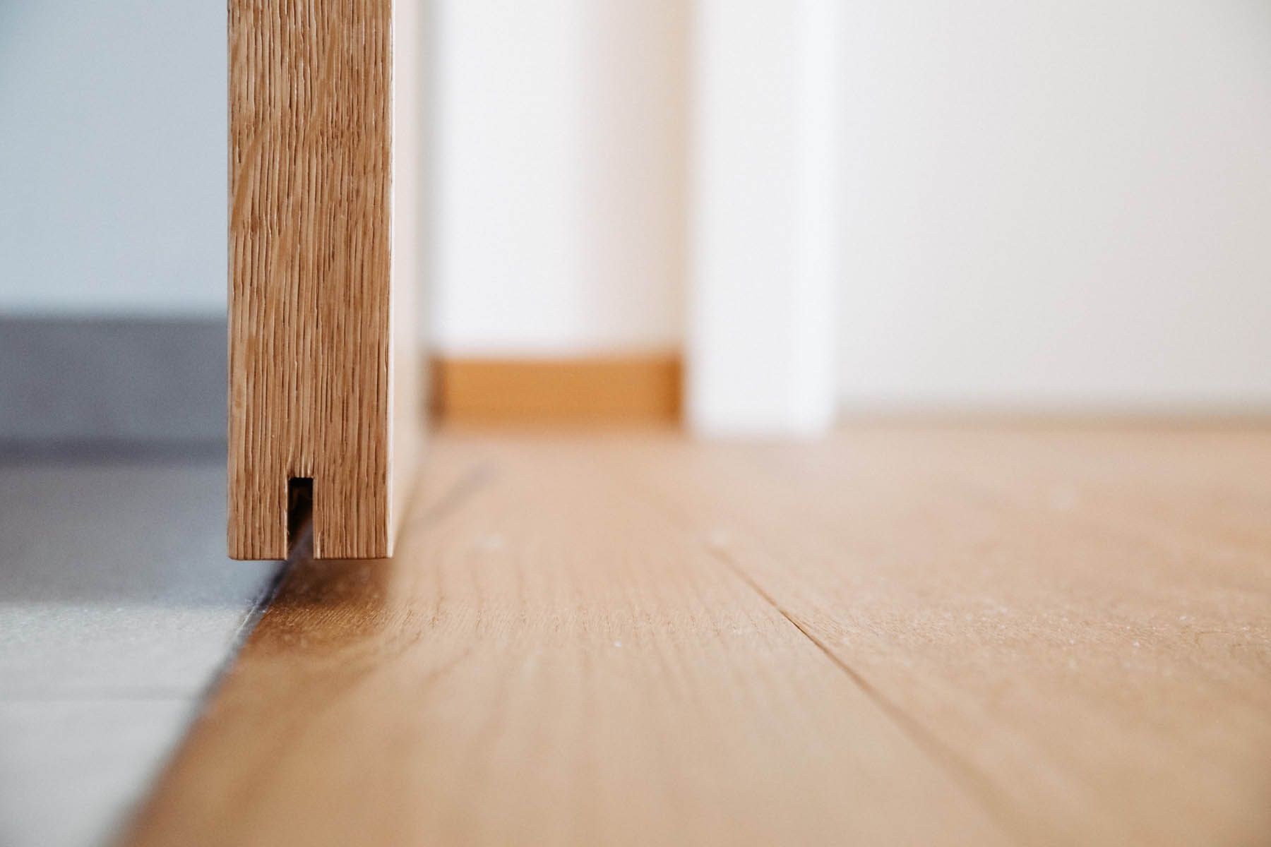 Holztürkante mit Schlitz, leicht geöffnet, über hellem Holzboden, vor einer weißen Wand.
