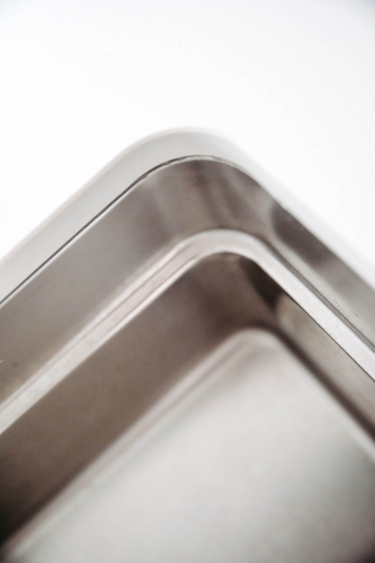 Nahaufnahme der abgerundeten Ecke eines Edelstahlbehälters vor einem strahlend weißen Hintergrund.