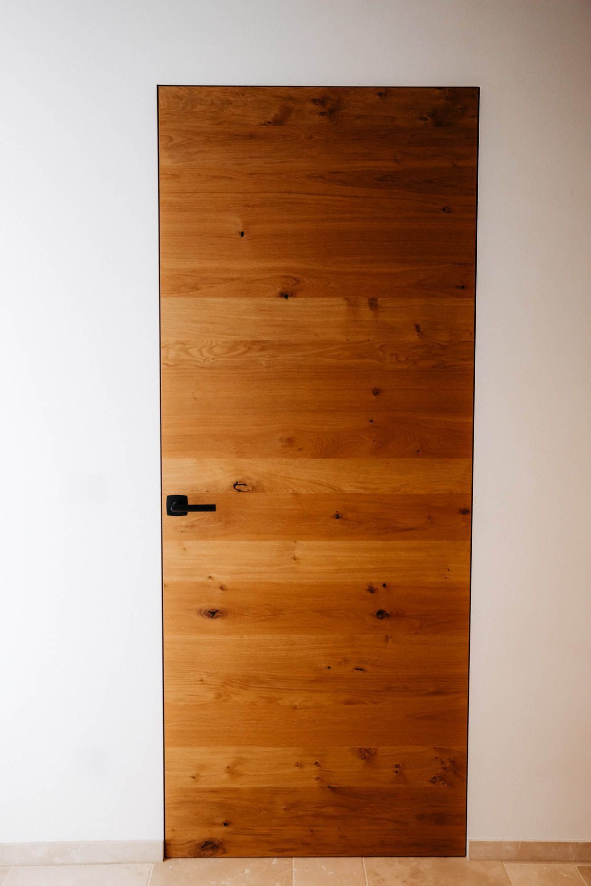 Holztür mit schwarzem Griff in einer weißen Wand.