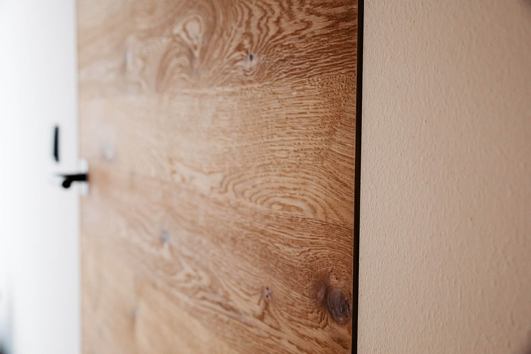 Holztür neben einer beigen Wand. Ein schwarzer Griff ist sichtbar.