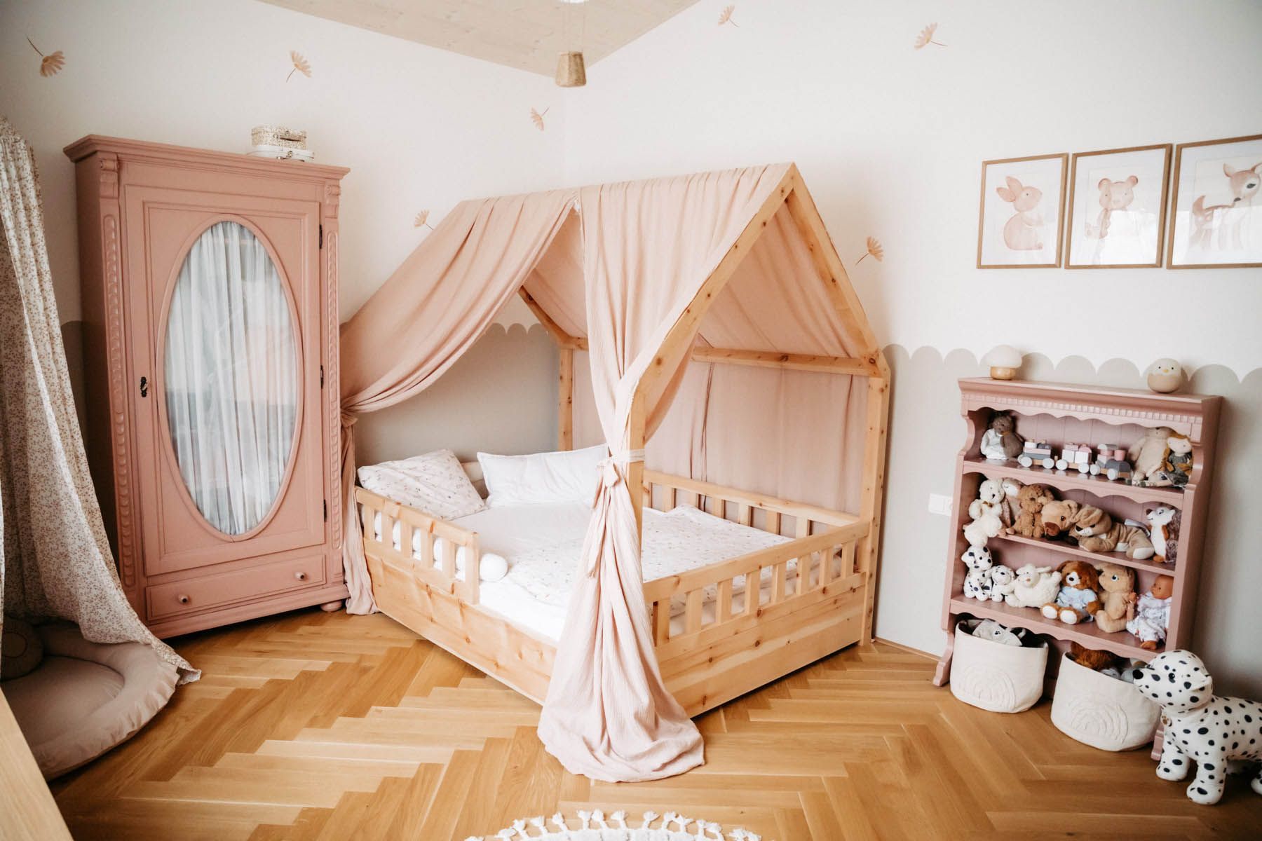 Kinderzimmer mit Himmelbett, rosa Kleiderschrank, Regalen mit Spielzeug und Holzboden.