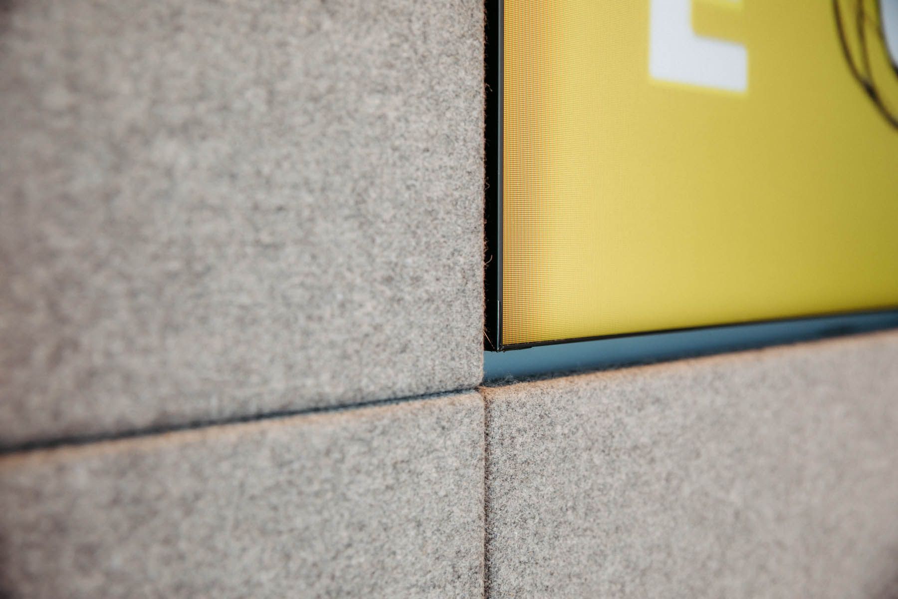 Nahaufnahme eines Bildschirms, der in eine mit grauen, strukturierten Paneelen verkleidete Wand eingelassen ist.