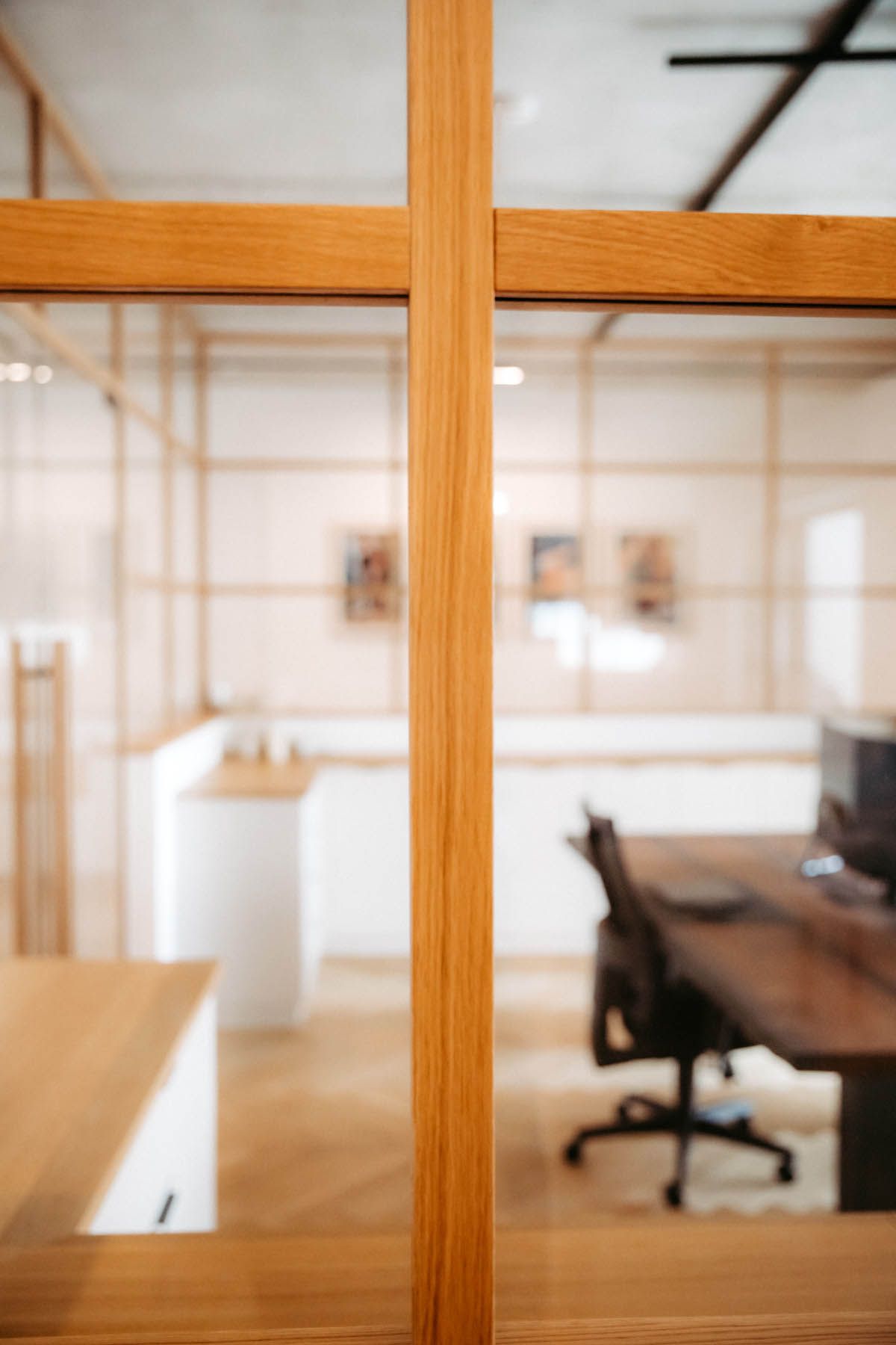 Bürotrennwand aus Glas mit Holzrahmen und verschwommenem Blick ins Innere eines Arbeitsbereichs.