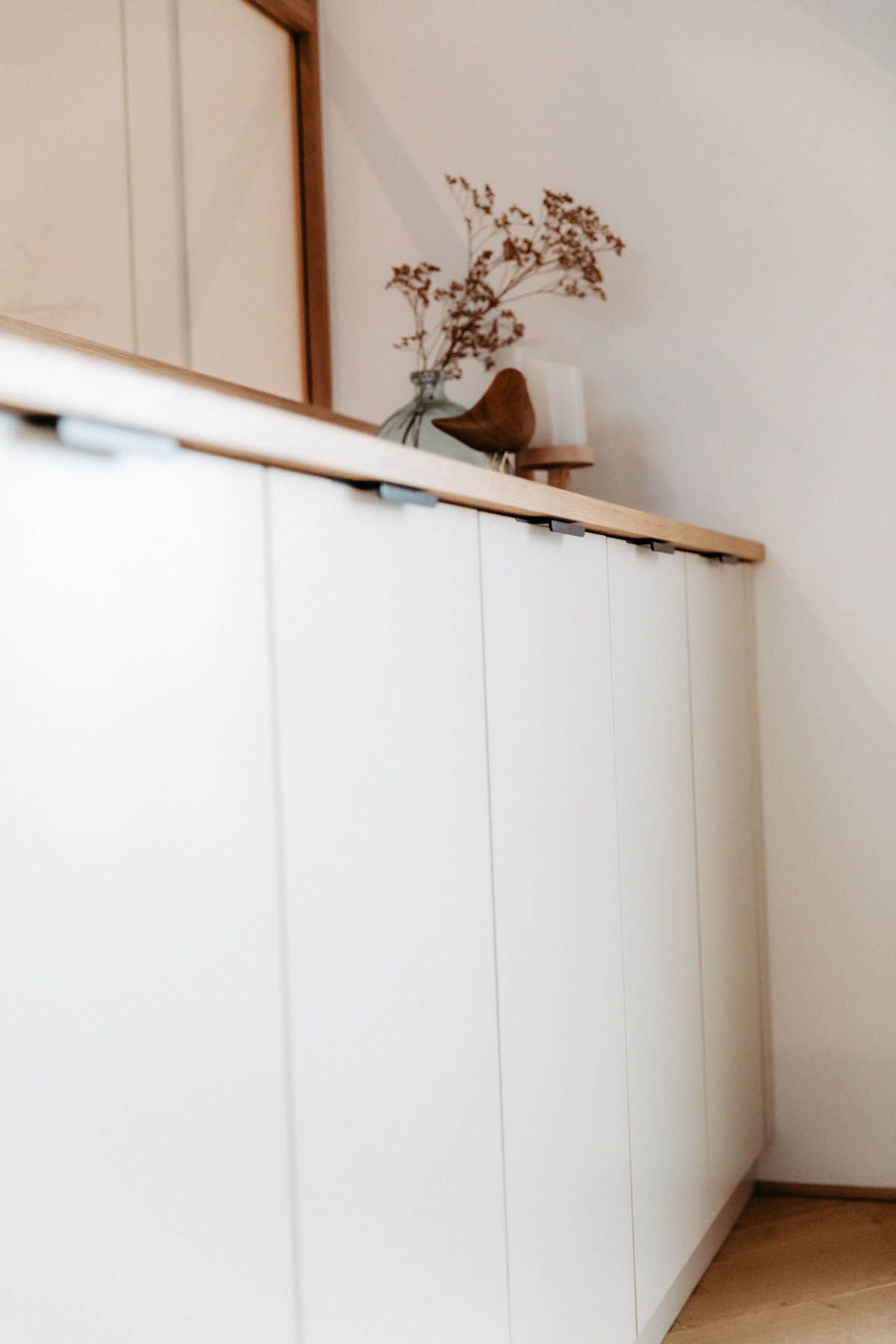 Weiße Schränke mit Holzarbeitsplatte, dekoriert mit getrockneten Blumen und einem Holzvogel.