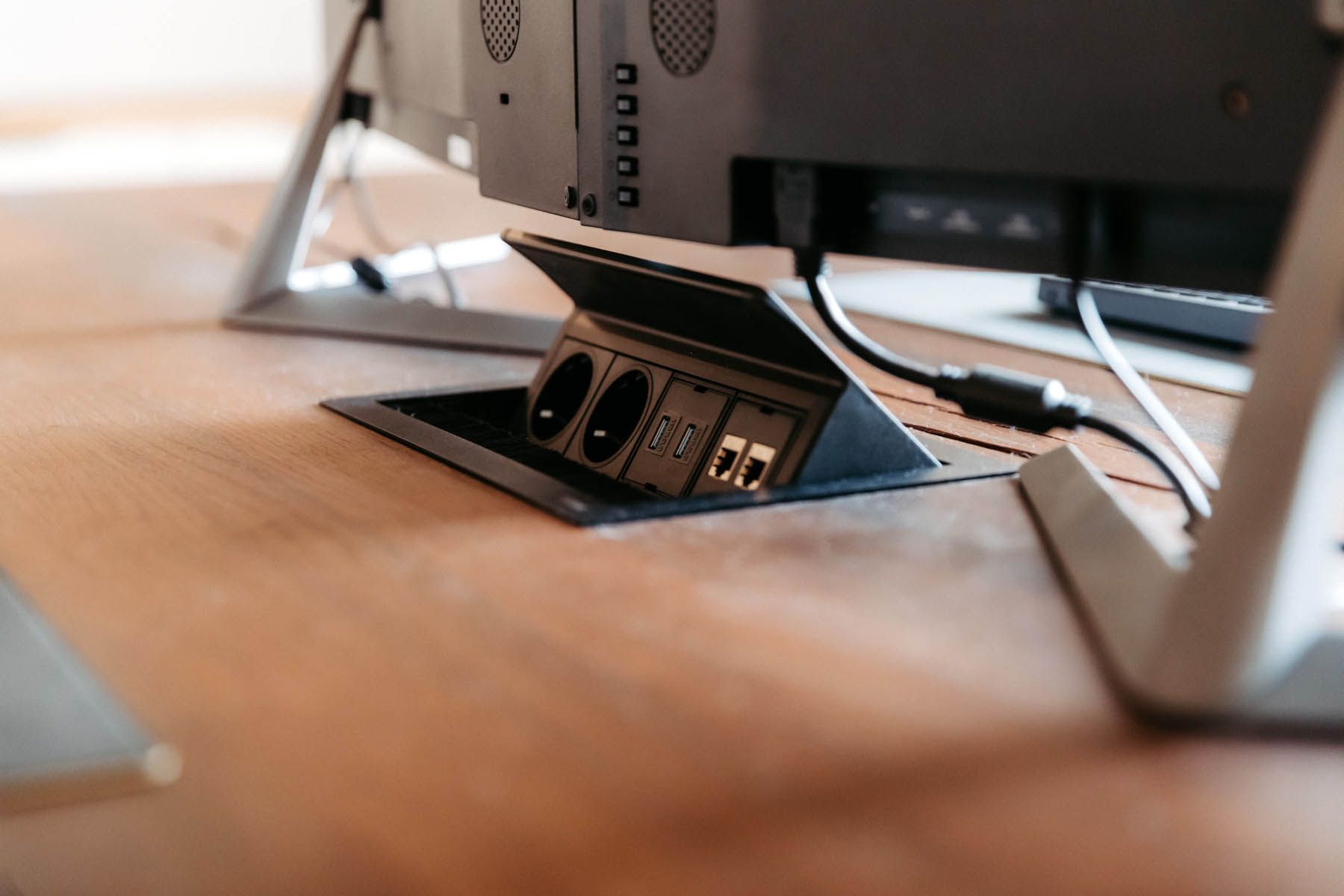 Steckdose im Holzschreibtisch installiert, Kabel und Computermonitor sind sichtbar.