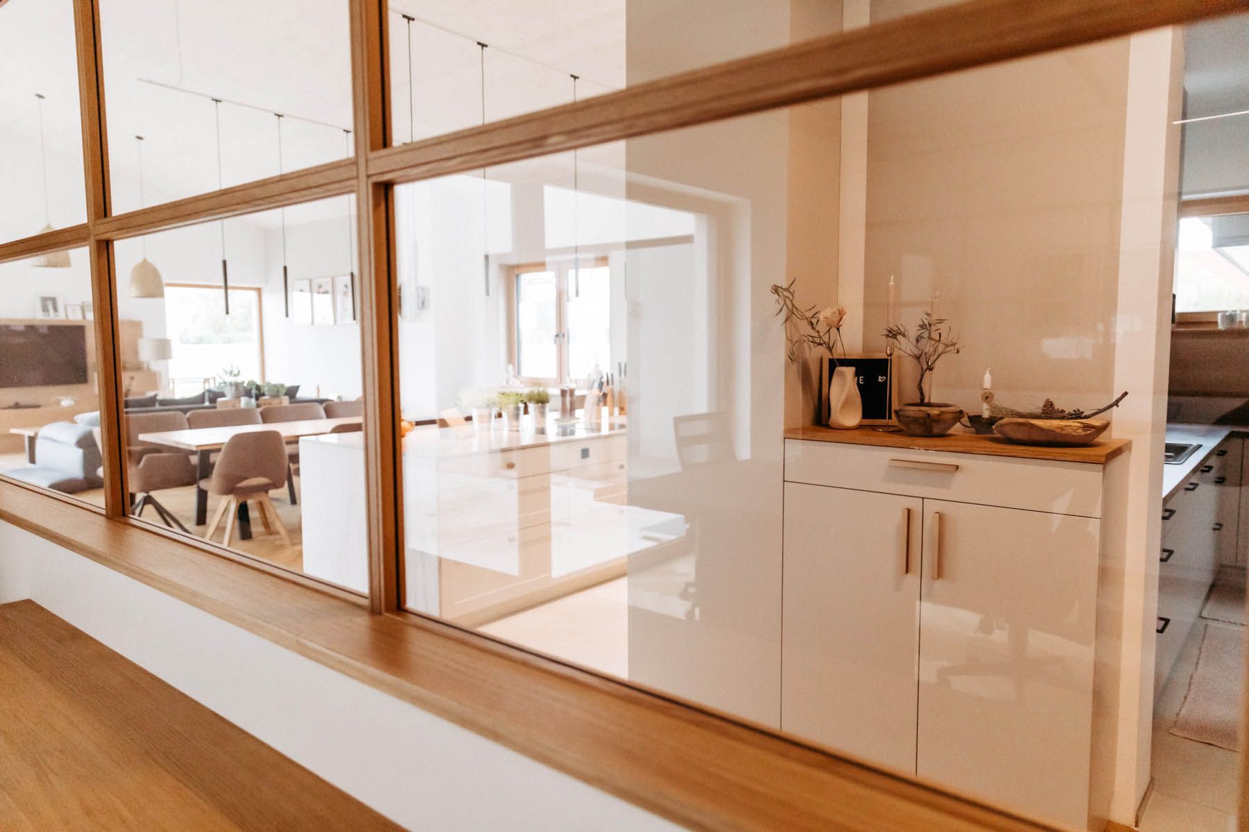 Küche mit Glaswänden und Holzrahmen; zeigt Essbereich und Küche mit weißen Schränken und Holzakzenten.