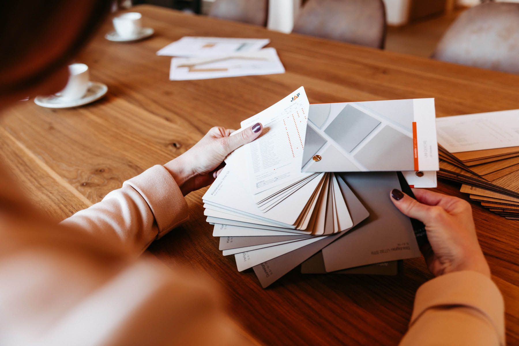 Frau am Holztisch, begutachtet Farb- und Materialmuster und wählt Designelemente aus.