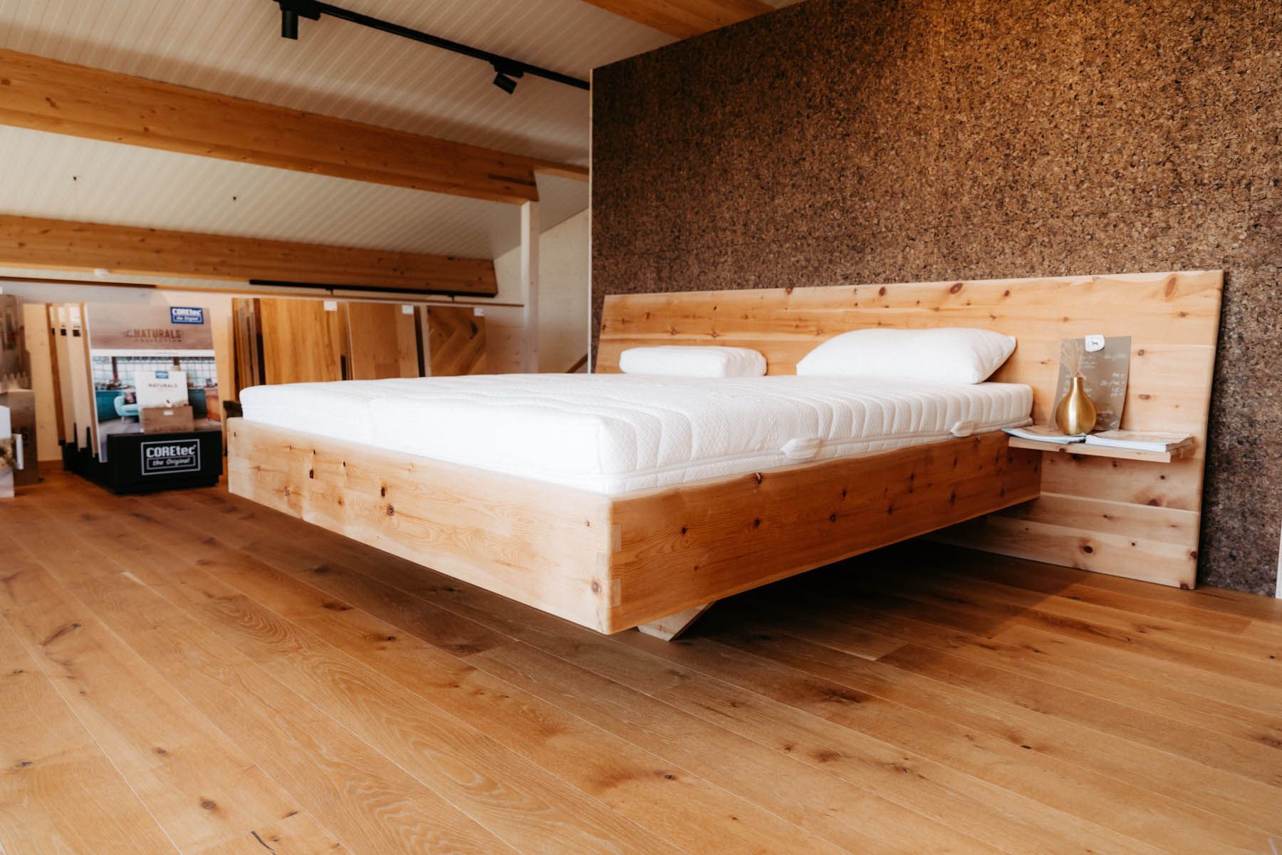 Holzbett in einem Ausstellungsraum mit Korkwandhintergrund und Hartholzböden.