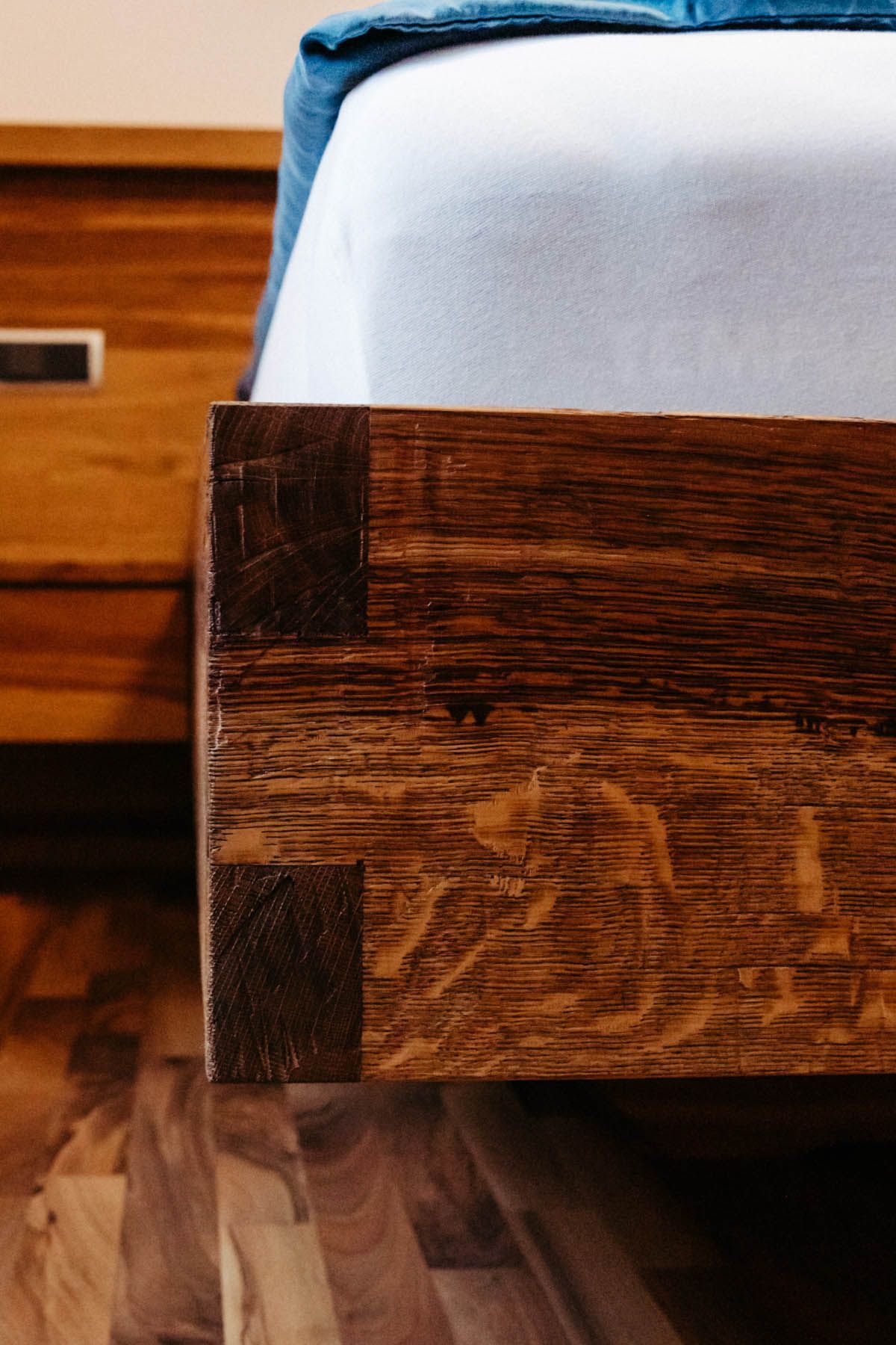Nahaufnahme eines hölzernen Bettrahmens mit Schwalbenschwanzverbindungen neben einem Nachttisch.