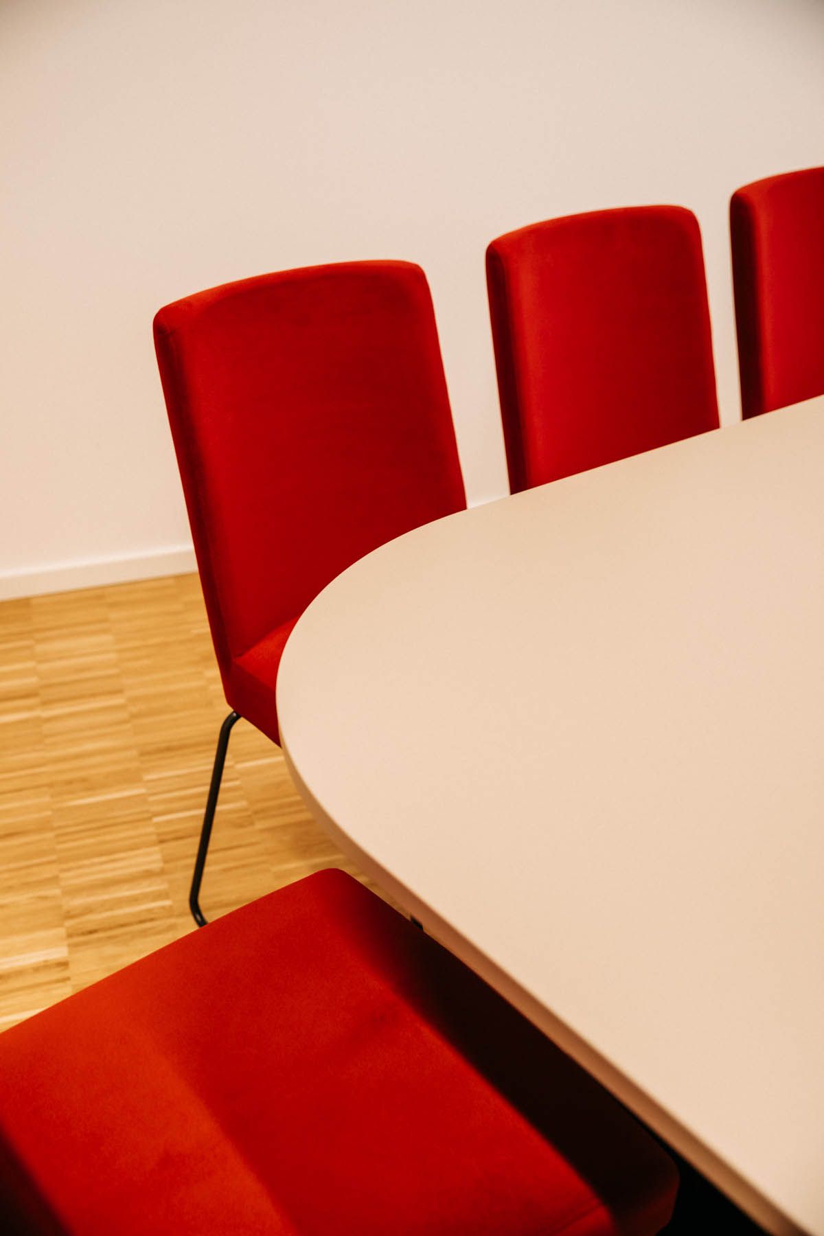 Rote Stühle um einen weißen Tisch in einem Besprechungsraum mit Hartholzboden.