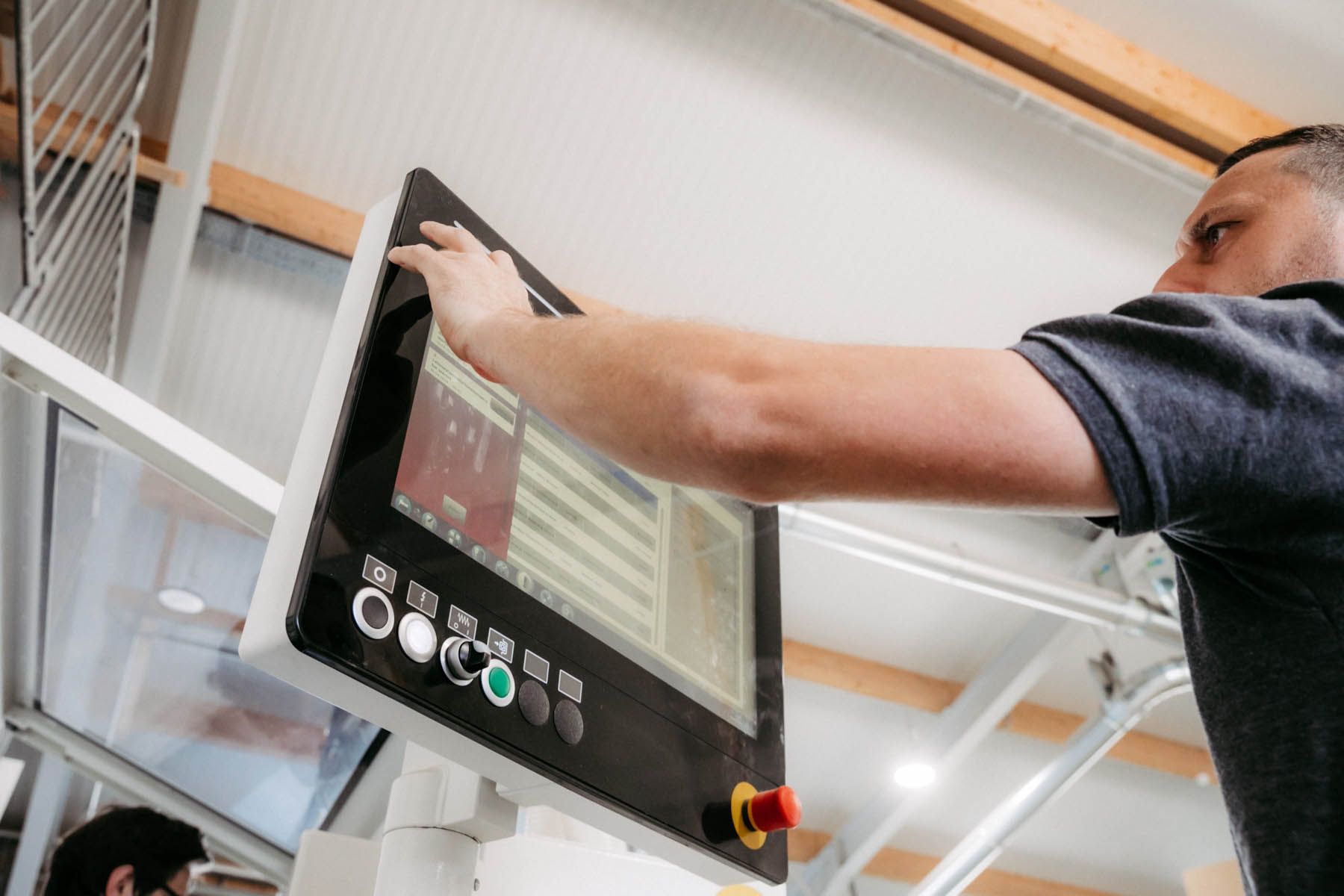 Mann bedient in einer Werkstatt einen Touchscreen. Er tippt auf den Bildschirm. Farben: Schwarz, Weiß und Silber.