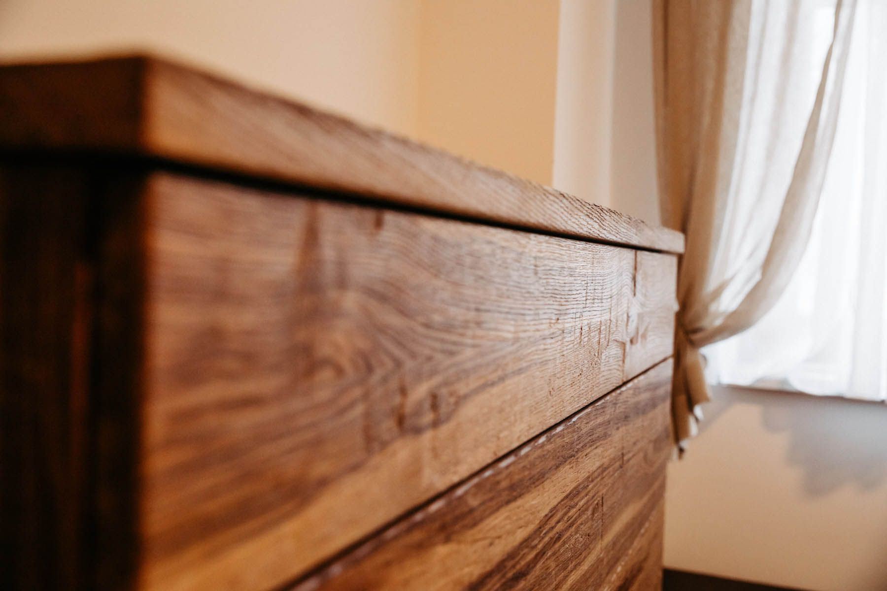 Nahaufnahme einer Holzkommode mit sichtbarer Holzmaserung neben einem durchsichtigen weißen Vorhang.
