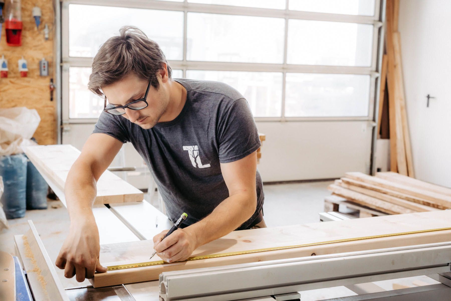 Mann mit Brille markiert in der Werkstatt Holz mit Bleistift und Lineal auf einer Tischkreissäge.