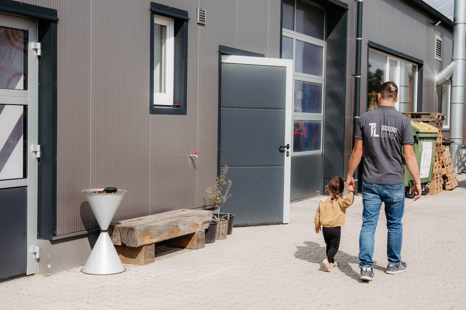 Mann und Kind gehen an einem grauen Gebäude vorbei. Der Mann hält die Hand des Kindes.