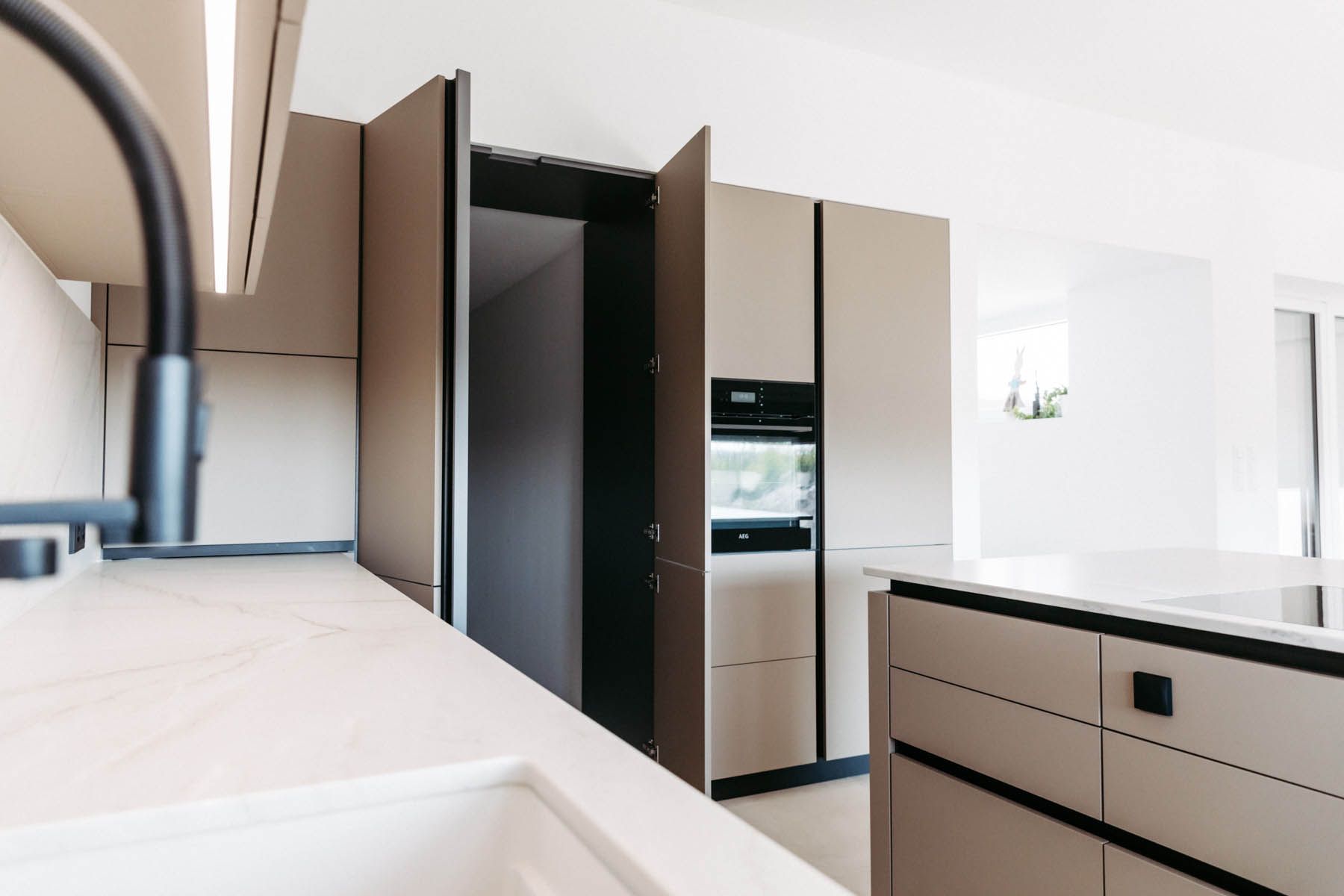 Moderne Küche mit hellen Schränken, schwarzen Akzenten und eingebautem Ofen, ein Schrank offen.