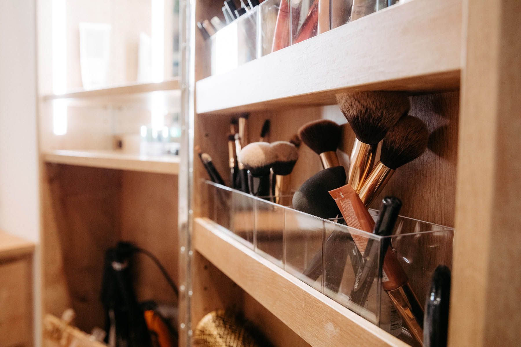 Make-up-Pinsel und -Produkte sind in einem hölzernen Schminktisch mit durchsichtigen Fächern organisiert.