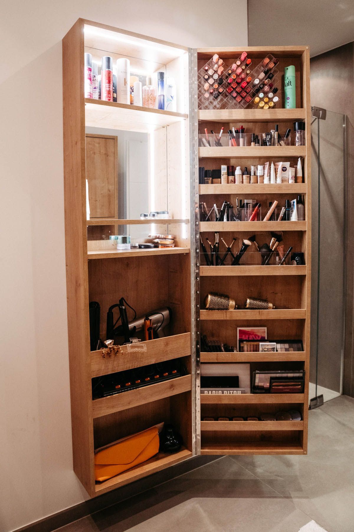 Offener Schminkschrank aus Holz, an der Wand montiert, mit Ausstellung verschiedener Kosmetikartikel, beleuchteter Innenraum.