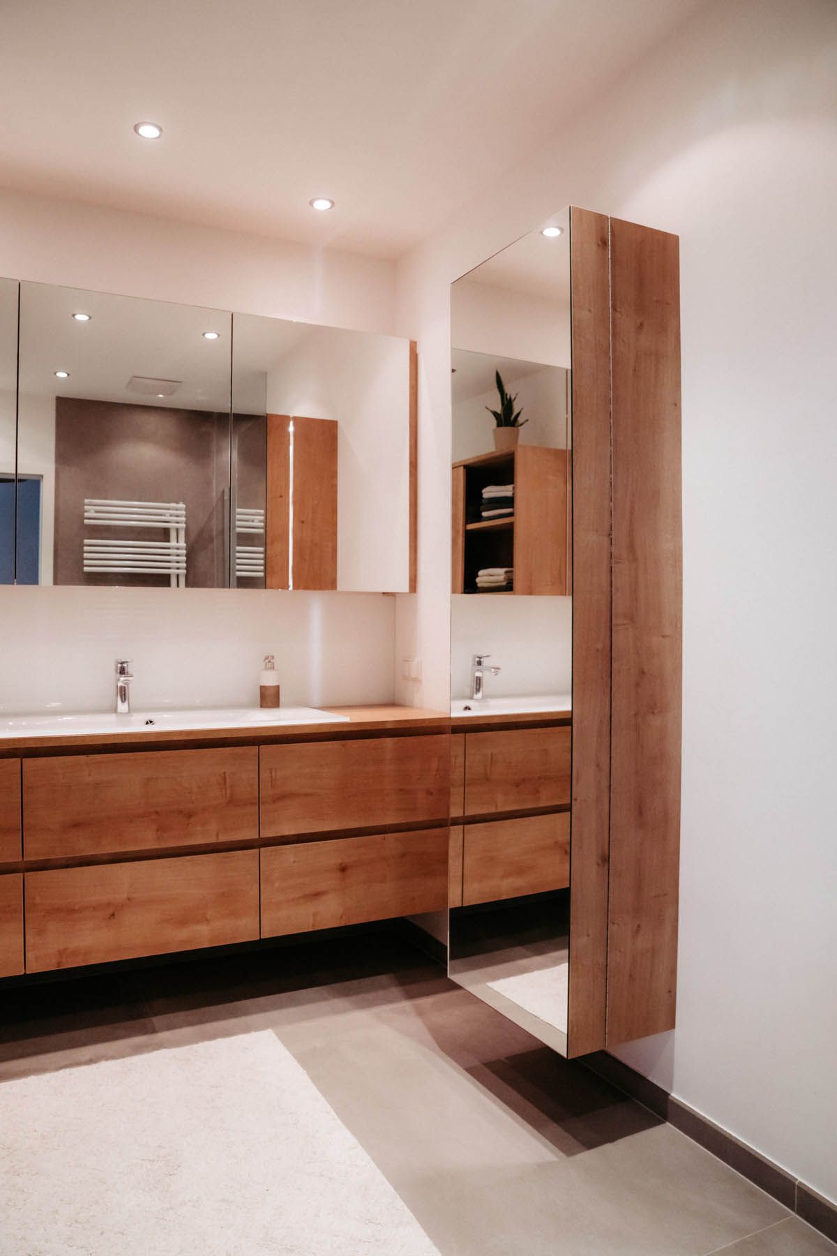 Modernes Badezimmer mit Holzwaschtisch, großem Spiegel und hohem Aufbewahrungsschrank mit Spiegel.