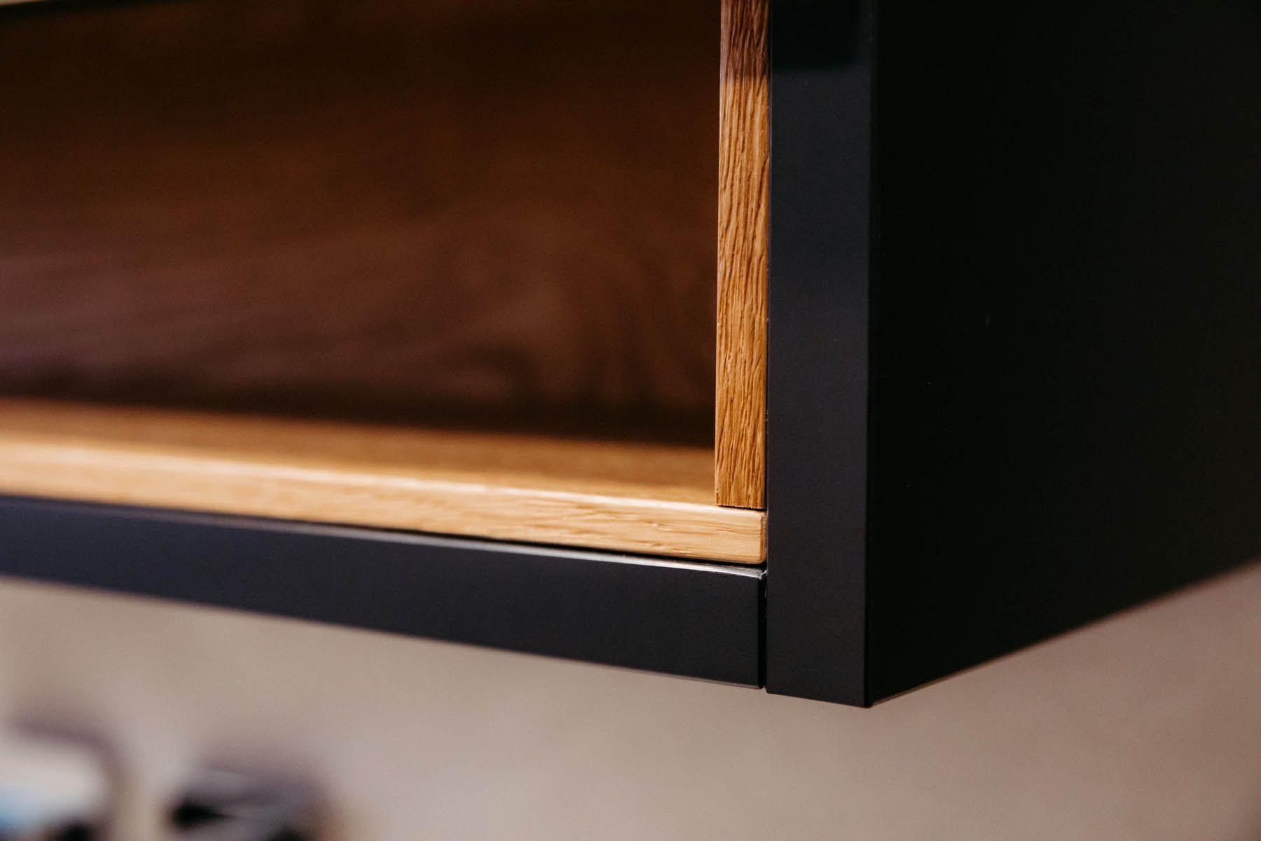 Schwarzes Regal aus Holz mit offenem Stauraum, an der Wand montiert.