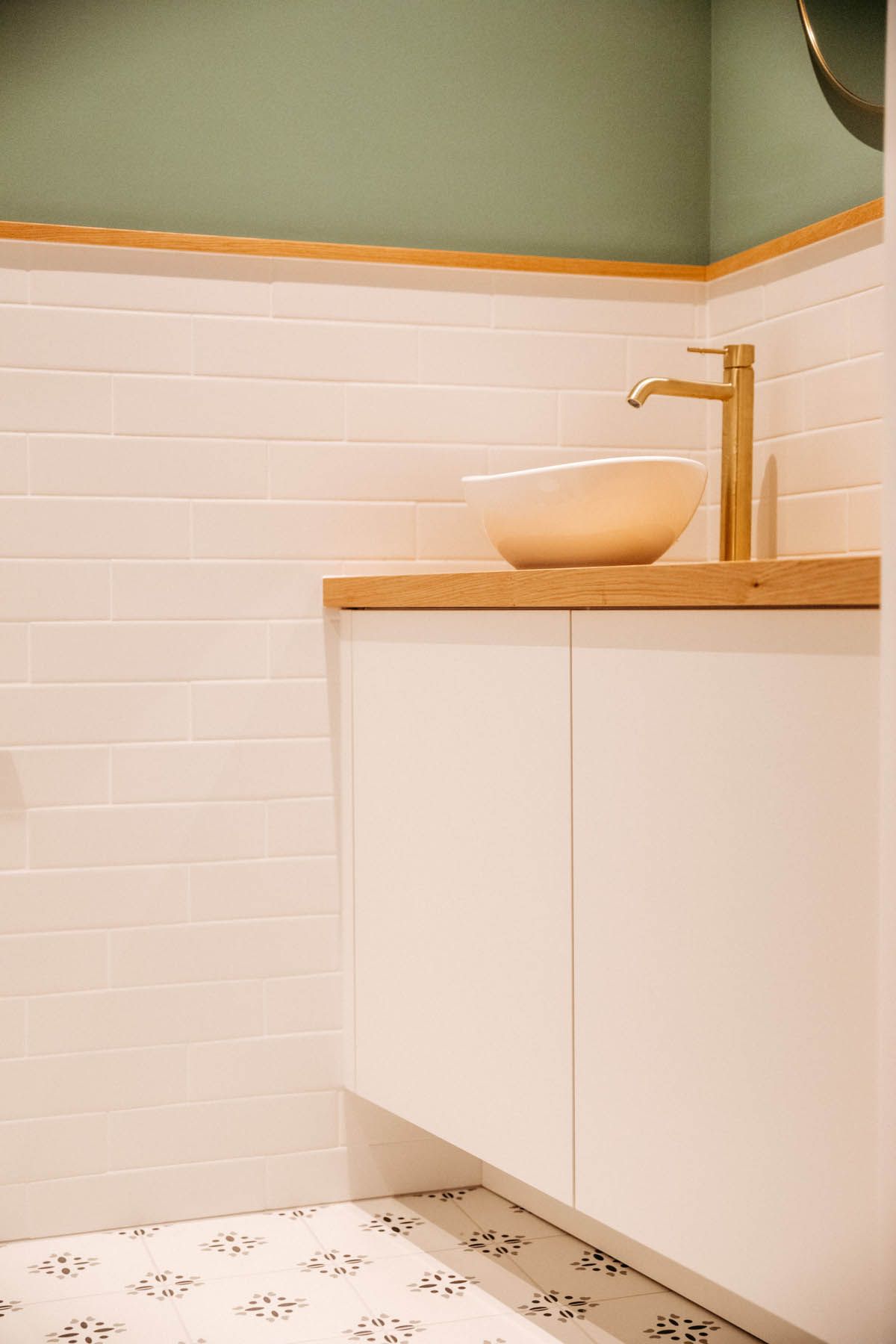 Weißer Badezimmerwaschtisch mit Aufsatzwaschbecken und goldenem Wasserhahn, weiße U-Bahn-Fliesen, grüne obere Wand.