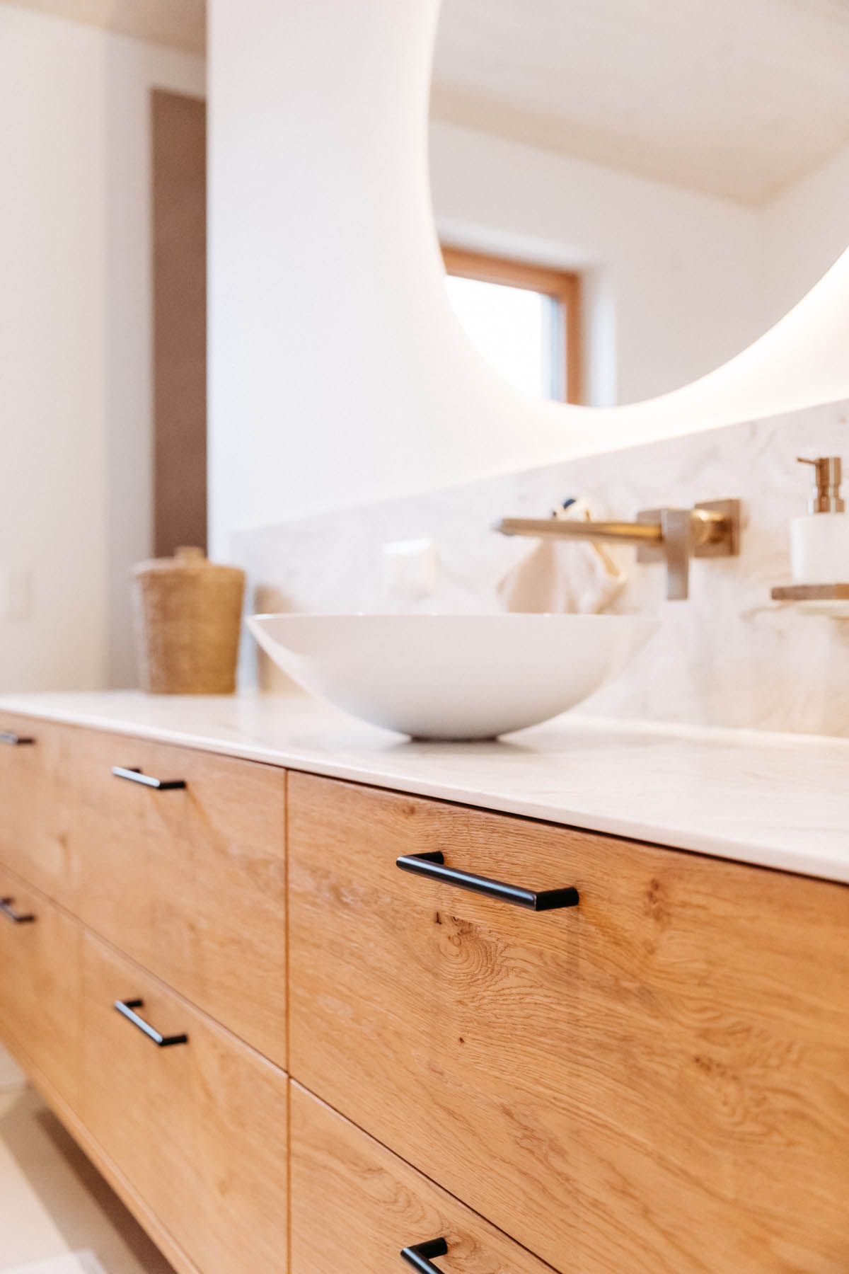 Badezimmerwaschtisch aus Holz mit weißem Waschbecken, schwarzen Griffen und goldenem Wasserhahn.