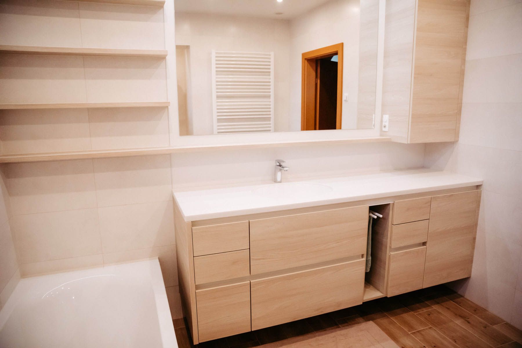 Modernes Badezimmer mit hellen Holzschränken, weißer Arbeitsplatte und großem Spiegel.