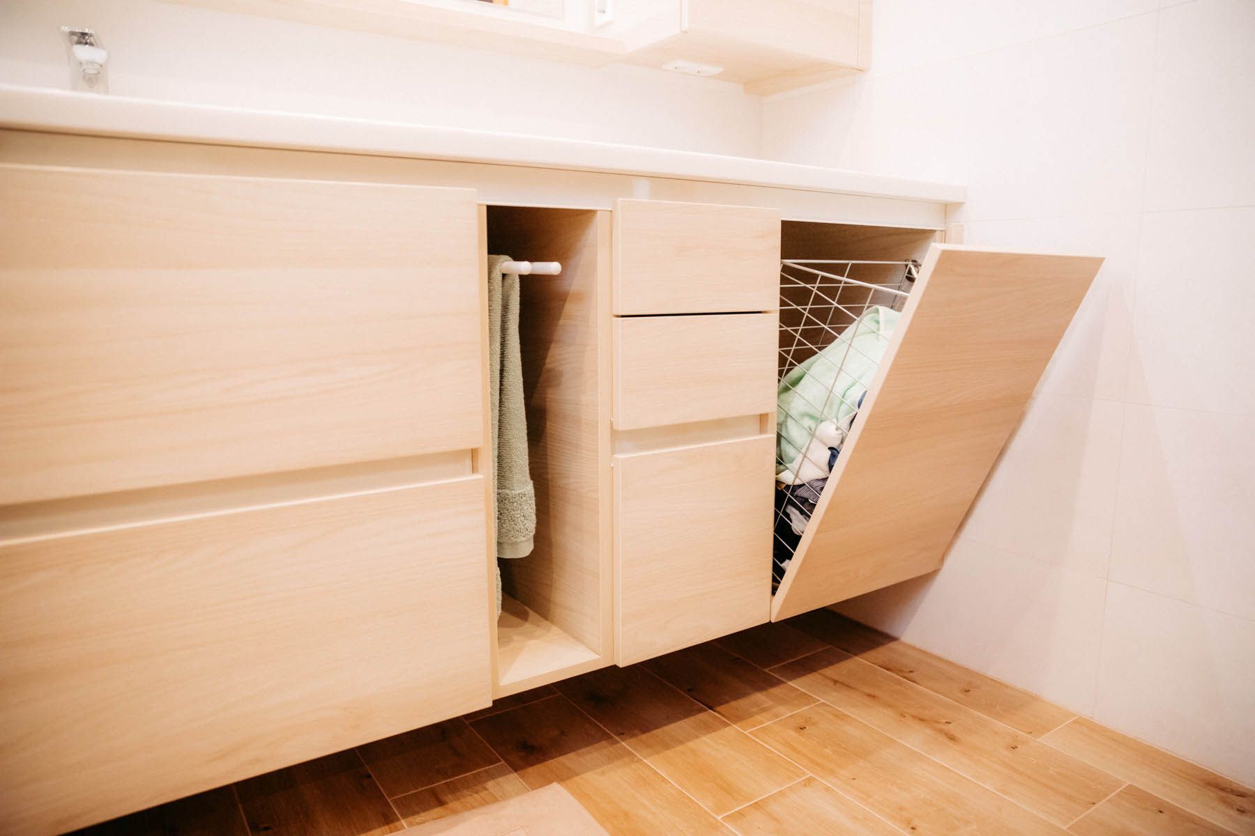 Wäscheschrank aus hellem Holz mit offenem Wäschekorb, Handtuchhalter und Schubladen.