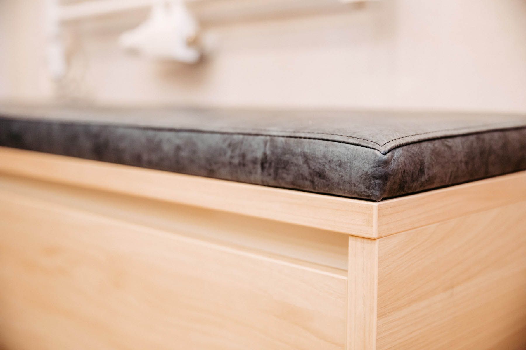 Eine Bank aus hellem Holz mit einer grauen, gepolsterten Oberseite.