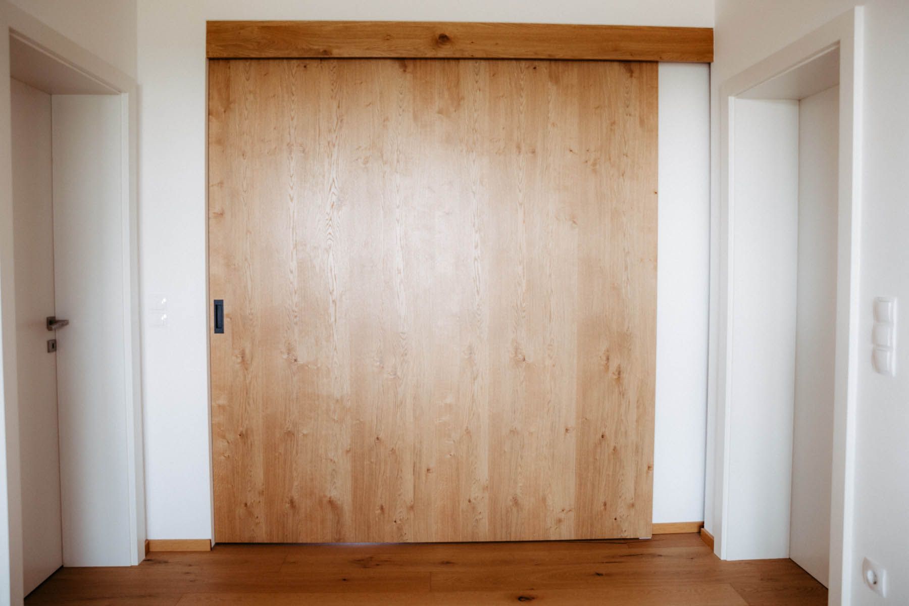 Hölzerne Schiebetür in einem Flur. Tür ist geschlossen, helles Holz, weiße Wände.