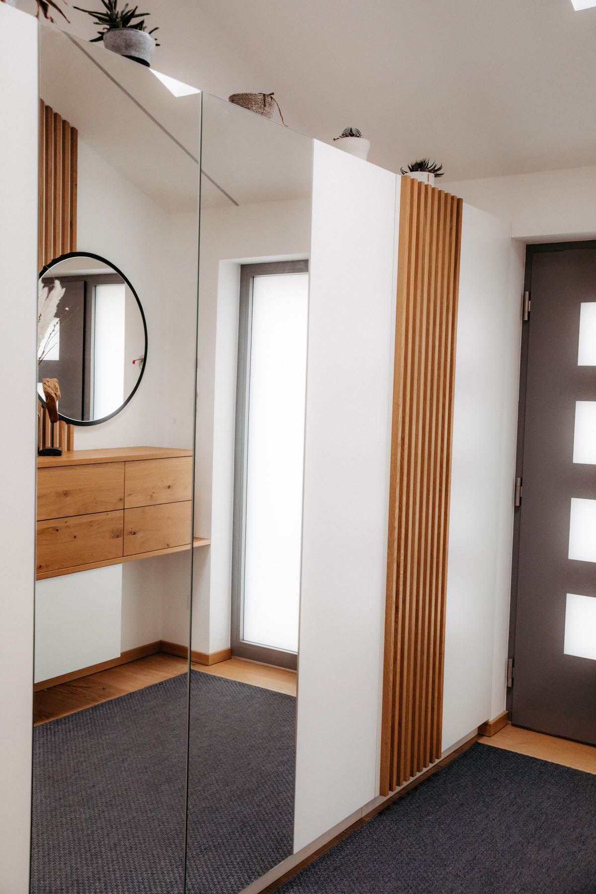 Eingangsbereich mit einer Akzentwand aus Holz, einem großen Spiegel, einer Holzkonsole und einem dunkelgrauen Teppich.