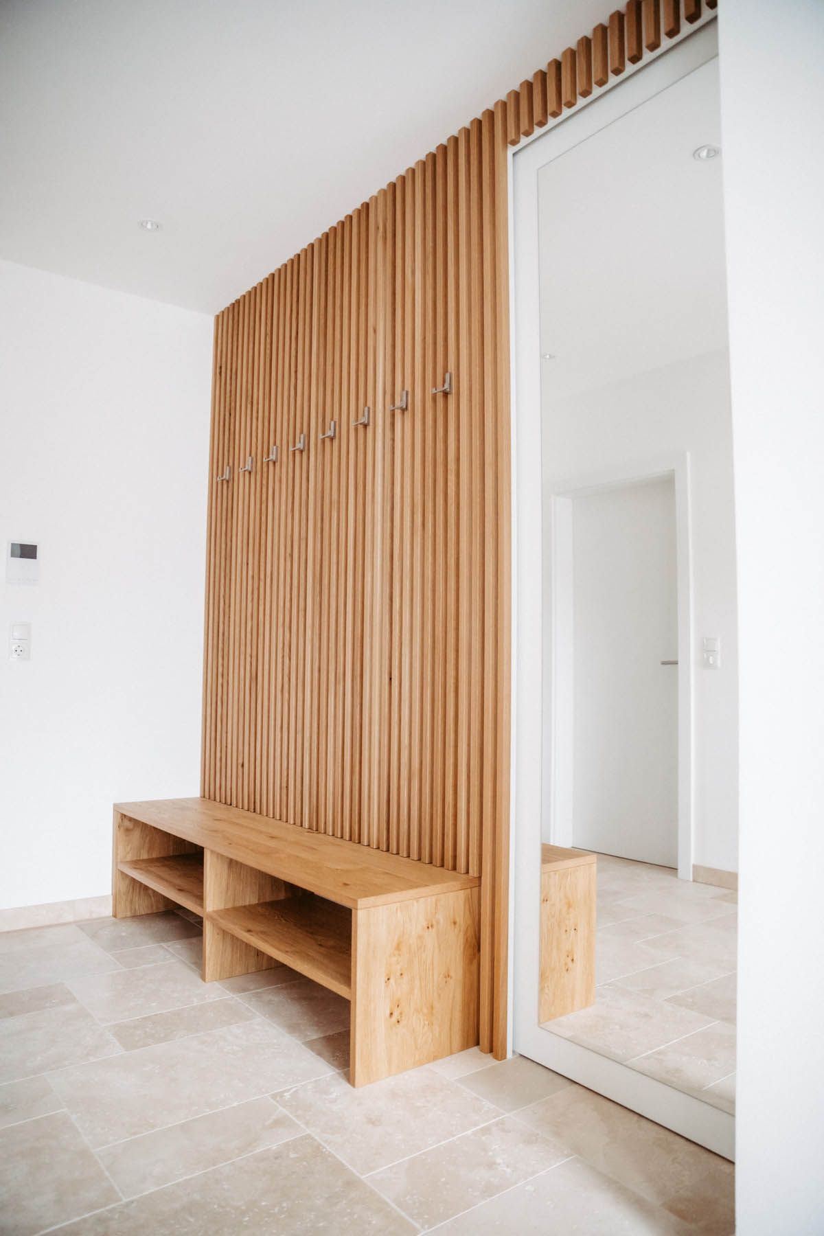 Hölzerner Eingangsbereich mit Bank, vertikaler Holzvertäfelung und einem großen Spiegel, der einen Türrahmen widerspiegelt.