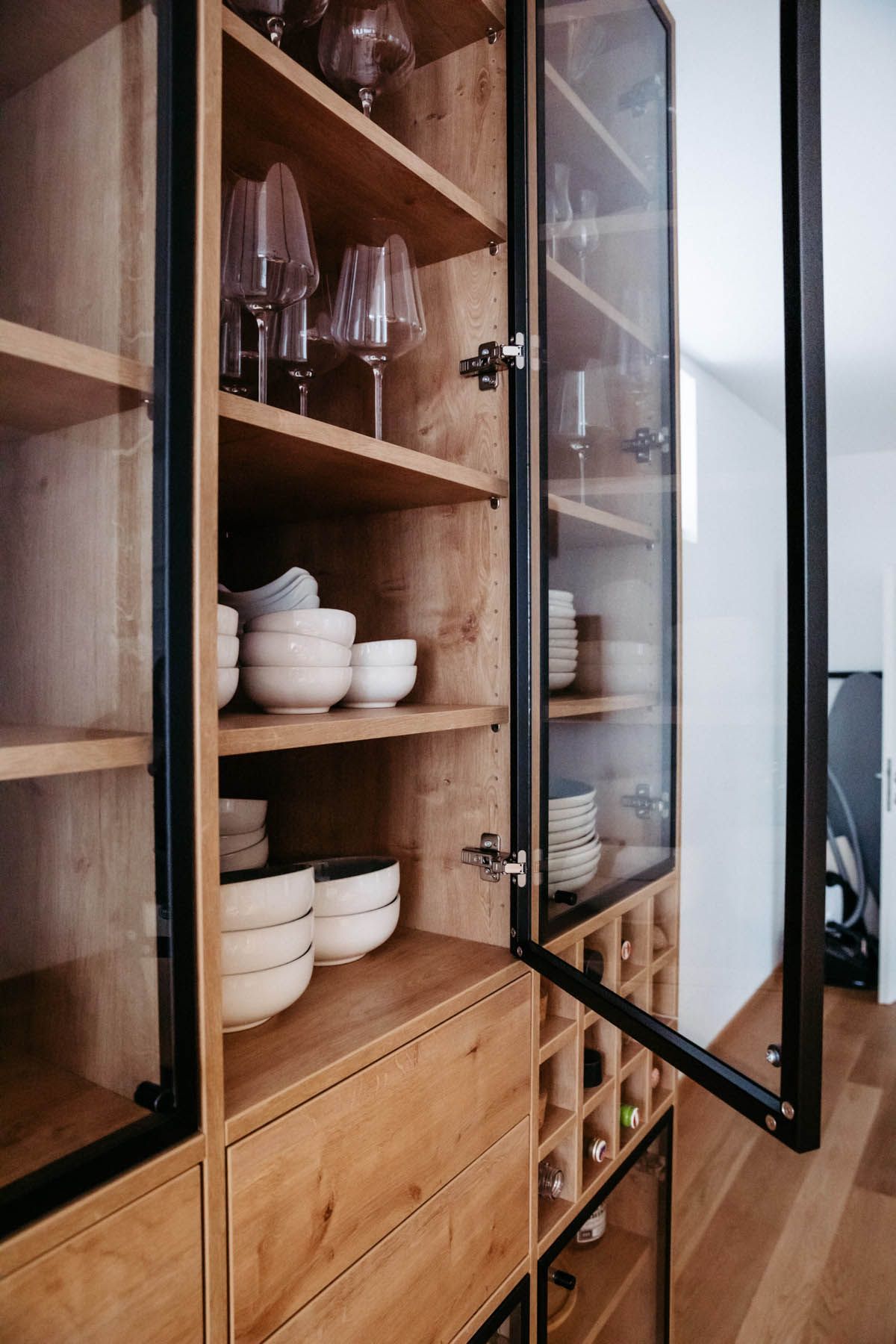 Holzschrank mit Glastüren zur Präsentation von Geschirr und Stielgläsern; darunter Weinlagerung.