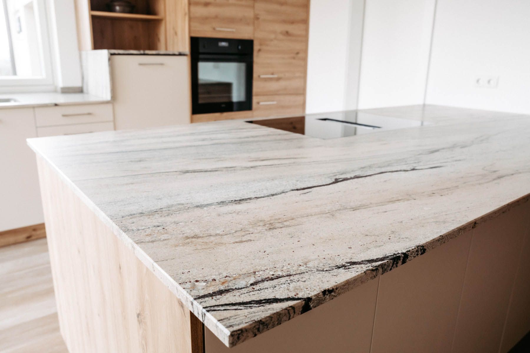 Kücheninsel mit heller Granitarbeitsplatte und eingebautem Kochfeld, helle Holzschränke.